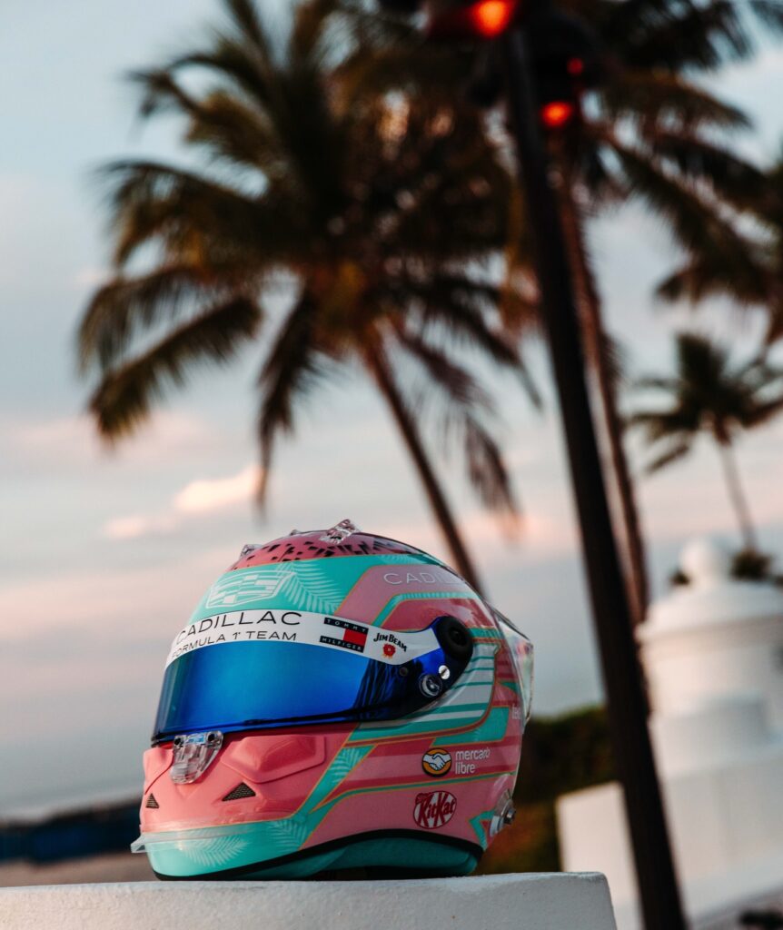 Sergio Pérez 2026 F1 Miami GP helmet — pink and teal Cadillac art deco livery, Tommy Hilfiger + Jim Beam visible, palm trees and Miami sunset backdrop