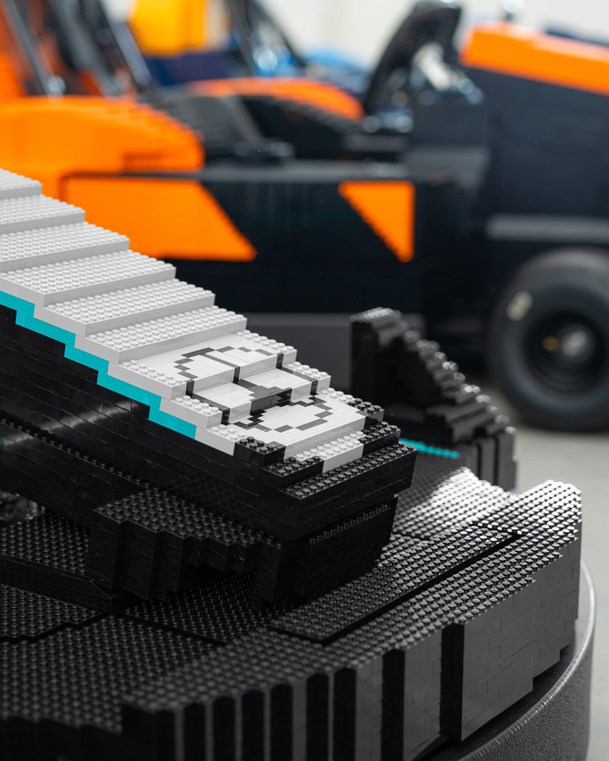 Close-up of the LEGO brick construction on a teal-and-silver Formula 1 show car, with an orange McLaren-liveried build behind.