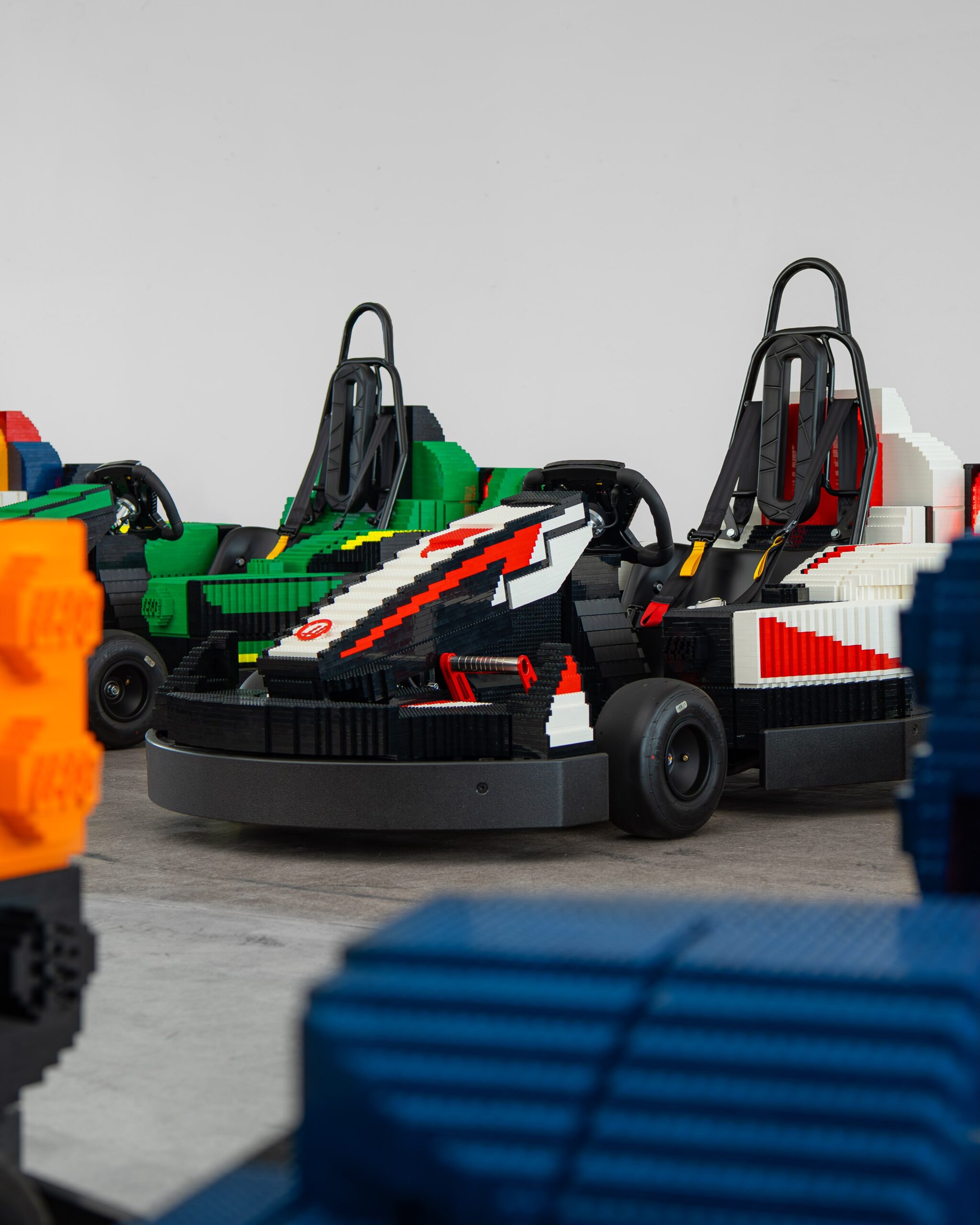 Ground-level view of several team-liveried LEGO Formula 1 cars showing racing seats, steering wheels and slick tyres.