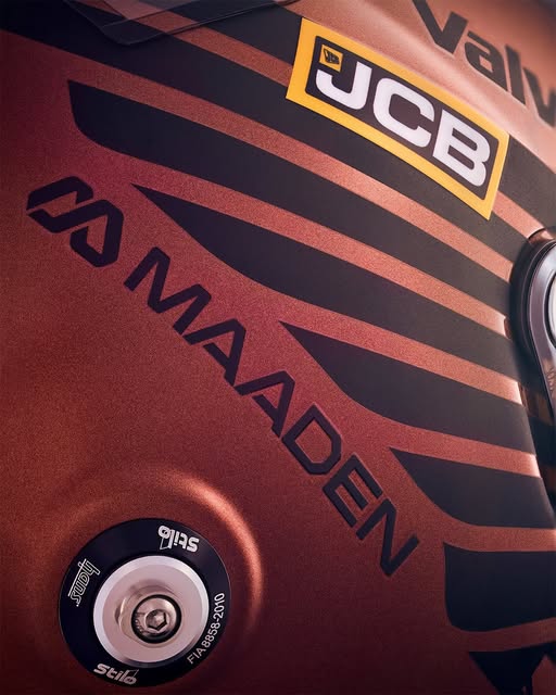 Lance Stroll 2026 Großbritannien GP Helm — Seitendetail schwarzer abgewinkelter Streifen und JCB/MAADEN Beschriftung auf metallischem Kupfer