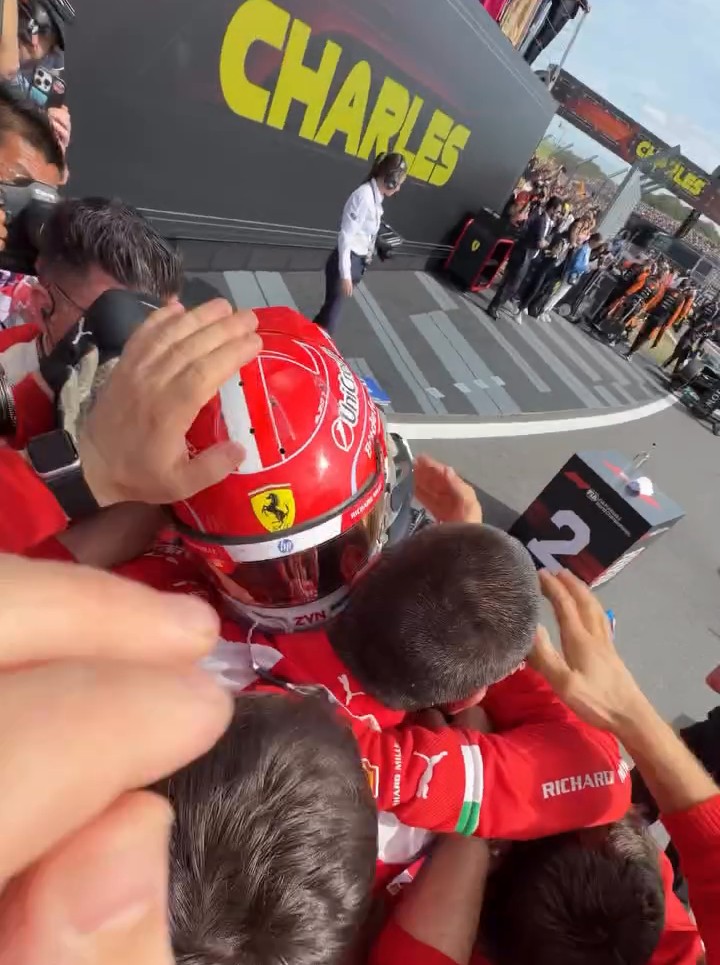 O capacete Ferrari vermelho #16 de Charles Leclerc enquanto a sua equipa celebra a sua vitória no Grande Prémio Britânico de 2026 em Silverstone