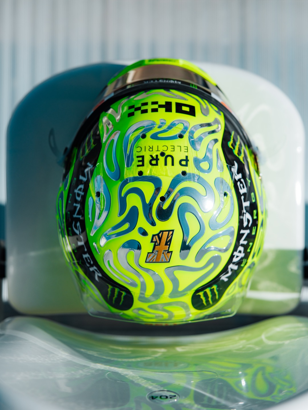 Lando Norris's fluoro-green 2026 British Grand Prix helmet covered in chrome liquid-metal blob swirls, with a Union Jack number badge.