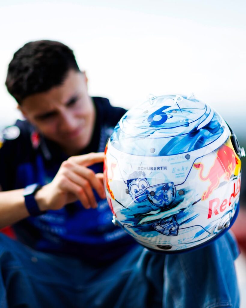 Isack Hadjar's 2026 Red Bull Racing helmet: cobalt brushwork on white, number 6 on the crown, physics equations and a cartoon on the rear