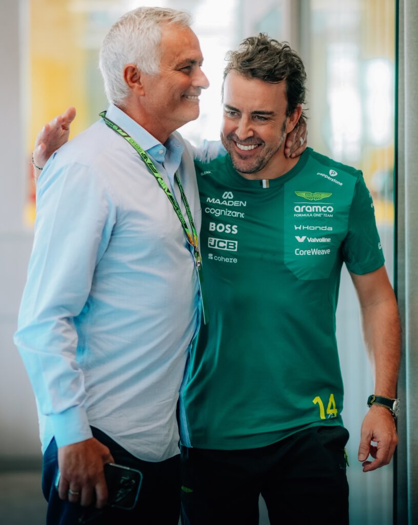 Fernando Alonso in Aston Martin team kit, smiling beside a team guest