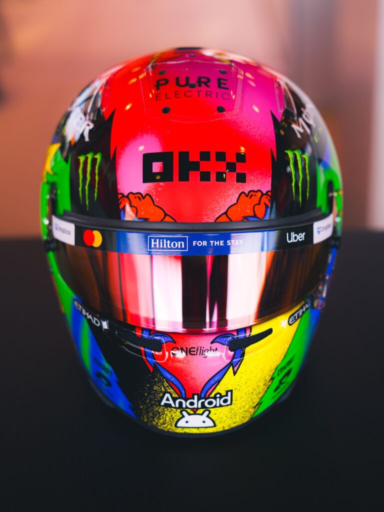 Lando Norris's 2026 Spanish GP helmet, front view: pop-art colour blocks with the OKX panel and Android chin marking