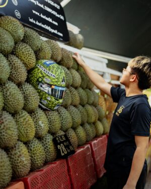 Three-quarter view of Alex Albon's green durian-skin Singapore GP helmet resting among durians on a fruit stall