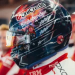 Lewis Hamilton's Austin 2026 helmet in profile: navy space scene with red and orange nebula, sketched white stars, chrome lines, gold mirrored visor