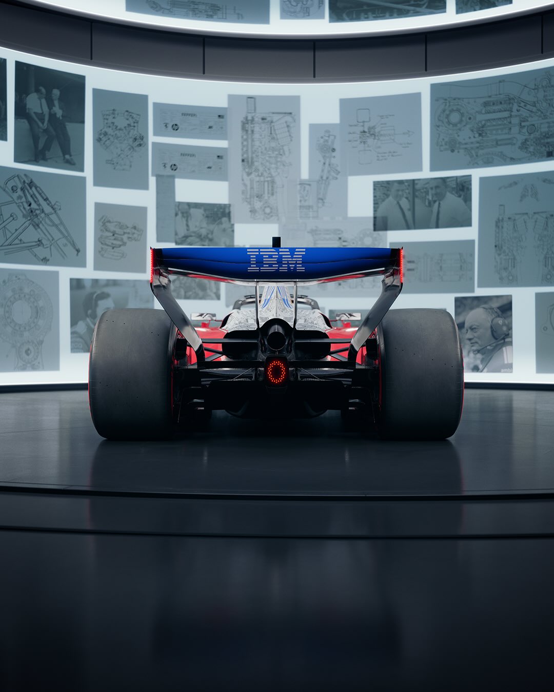 Rear of the Ferrari SF-26 with a blue IBM rear wing, in front of a wall of archive drawings