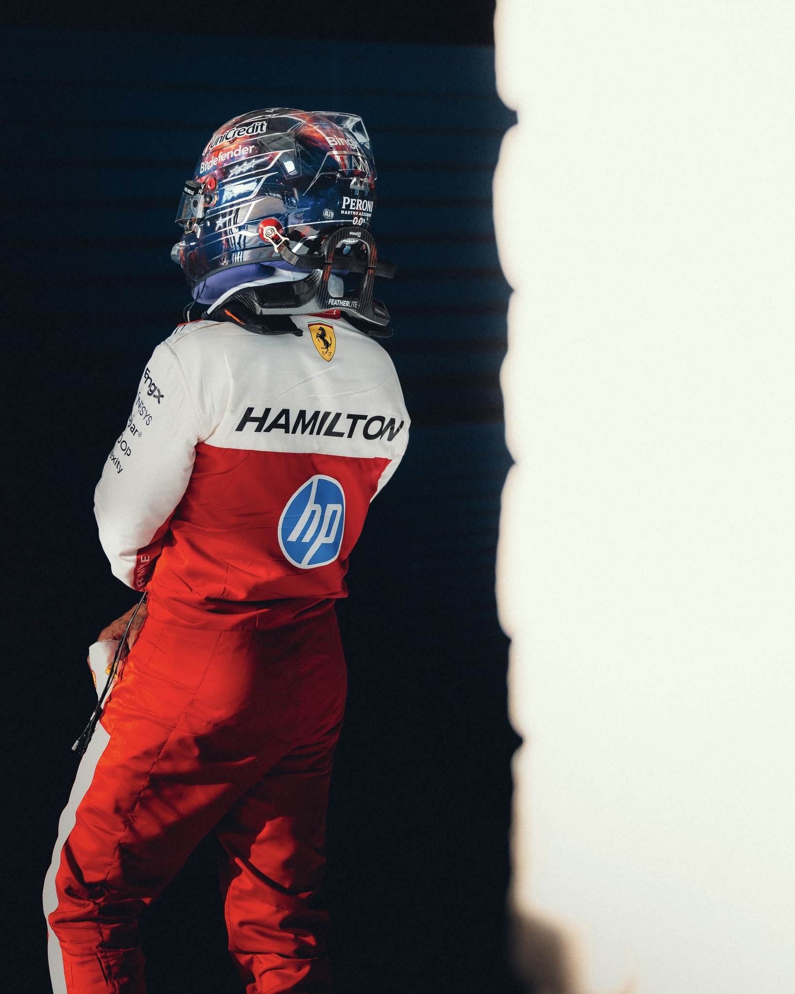 Lewis Hamilton from behind in his white and red Ferrari race suit, wearing his Austin 2026 helmet