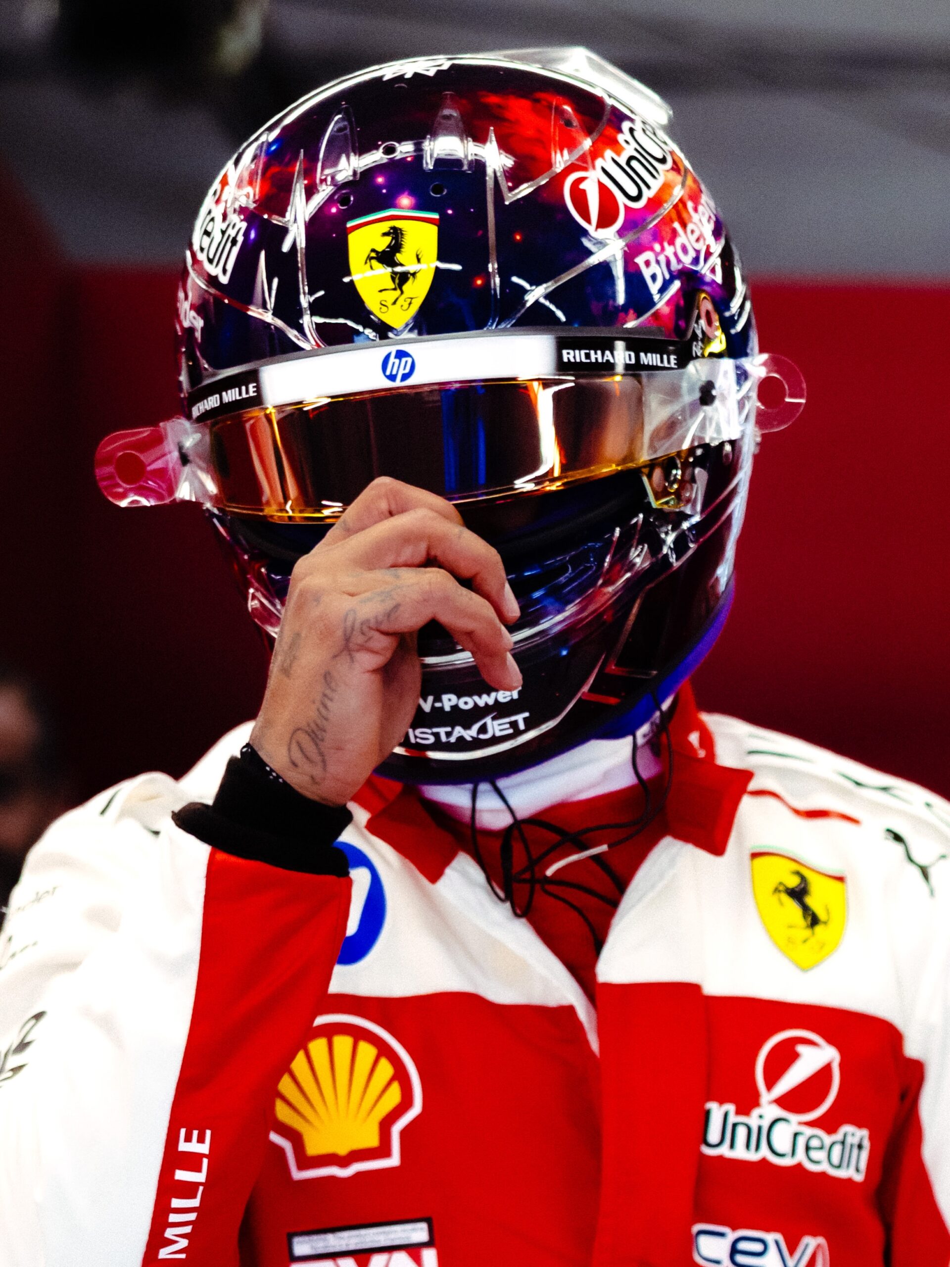 Lewis Hamilton's Austin 2026 helmet from the front, worn: Ferrari shield on the space-scene shell, gold mirrored visor under a strip with HP and RICHARD MILLE