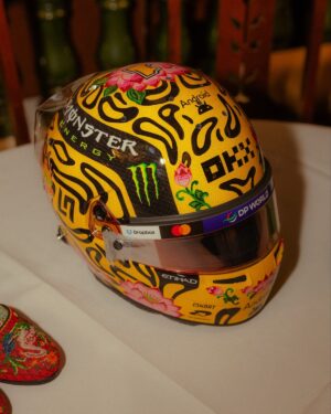 Three-quarter front view of Lando Norris's yellow 2026 Singapore GP helmet with black blobs, pink lotus flowers, Monster Energy and OKX