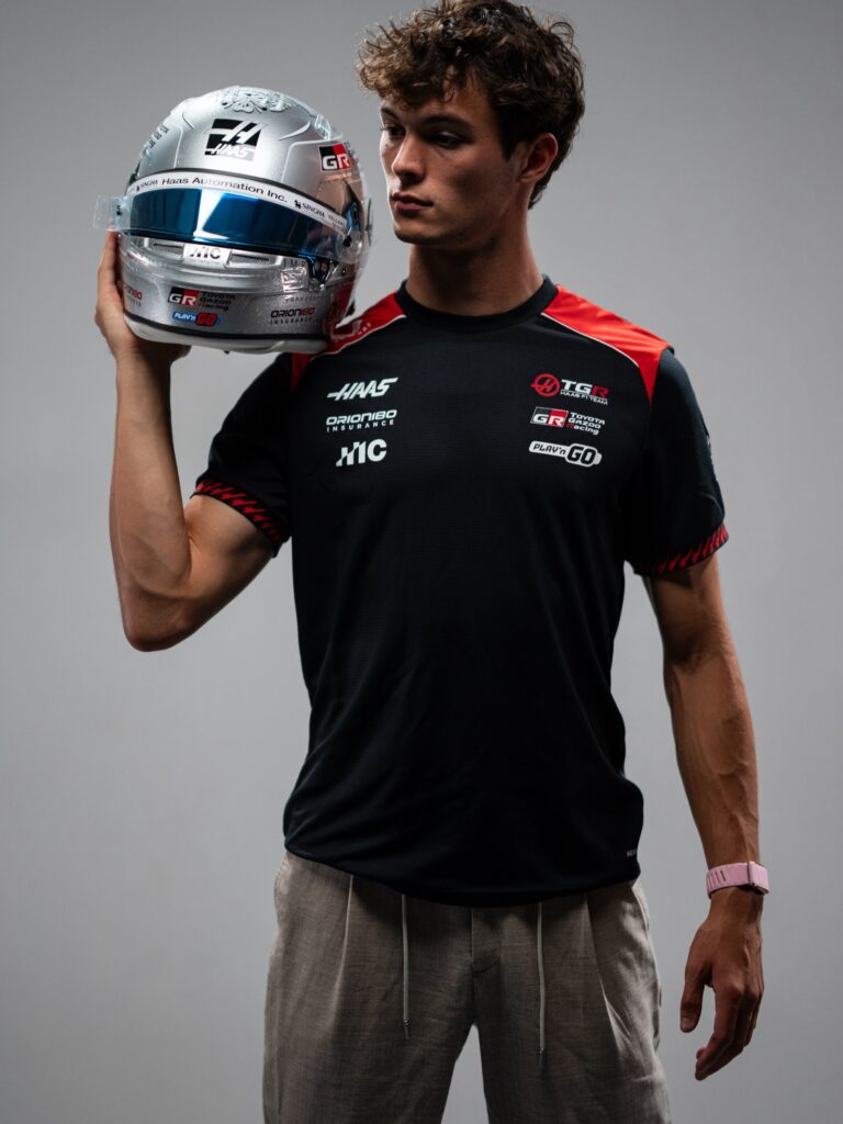 Oliver Bearman in a TGR Haas F1 Team shirt holding his silver 2026 Singapore GP helmet with a blue mirrored visor