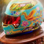 Oscar Piastri's turquoise 2026 Singapore GP helmet on a carved wooden stand: beaded phoenix, peonies and the name Oscar