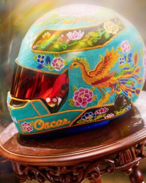 Oscar Piastri's turquoise 2026 Singapore GP helmet on a carved wooden stand: beaded phoenix, peonies and the name Oscar